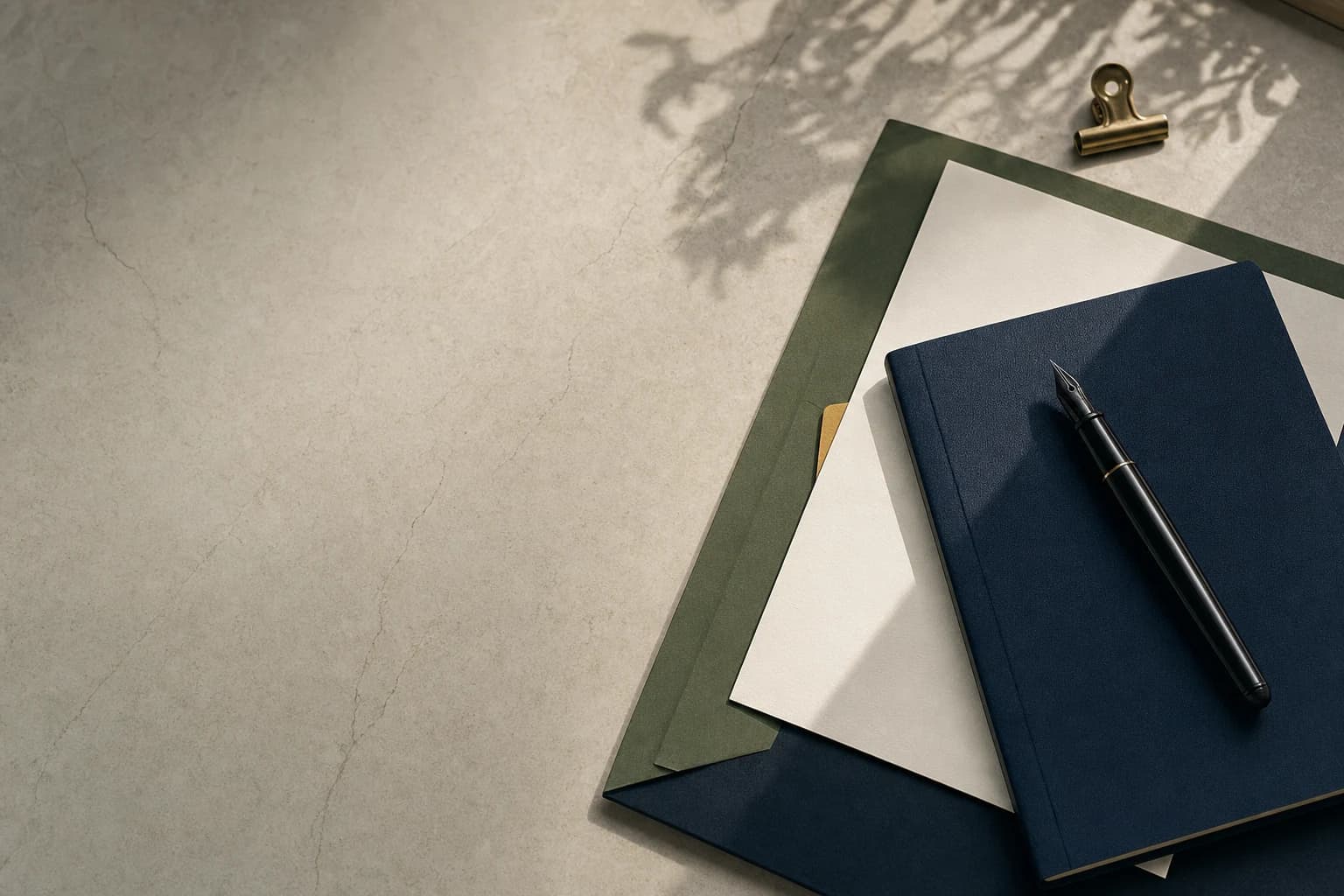 A dark notebook, pen, and paper arranged on a quiet stone desk